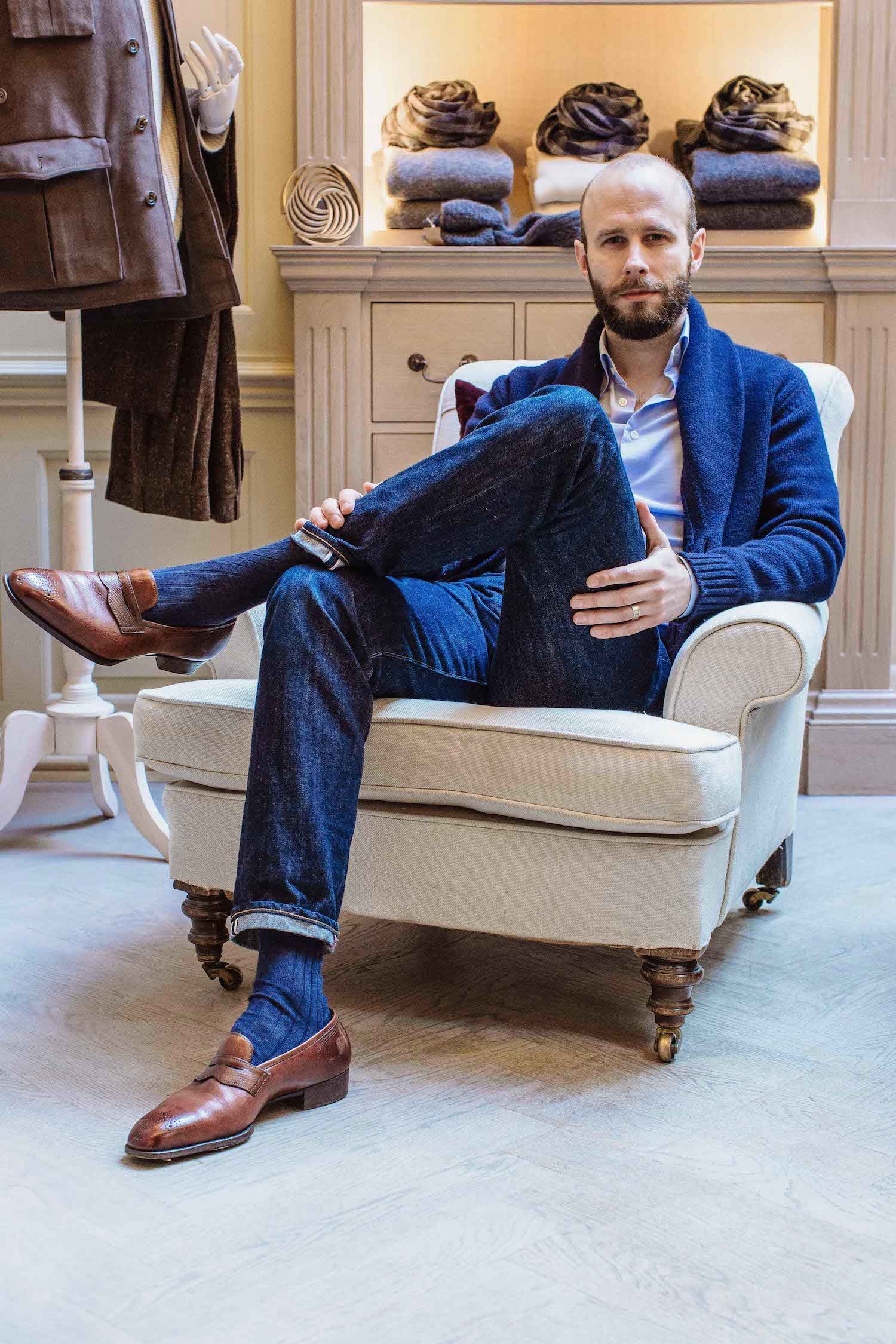 Une variation en smart-casual élaborée à partir d’un luxueux cardigan en maille bleu marine couvrant nonchalamment une chemise oxford bleu ciel à col boutonné, de  l’indispensable jean selveldge brut et de mocassins marron patinés par le temps. A la fois chic et moderne, ce look devrait vous permettre de passer relativement inaperçu, tout en ayant pour plusieurs milliers d’euros de frusques sur le dos. Source : Permanent Style.