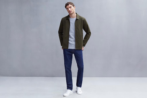 Un look casual qui allie blouson en coton vert militaire, t-shirt gris clair débordant sur jean brut semi-slim et sneakers minimalistes blanches. Conseil de style : usez un peu et ajoutez un gilet jaune ; vous êtes prêt pour aller casser du sartorialiste. Source : @sunspelclothing.