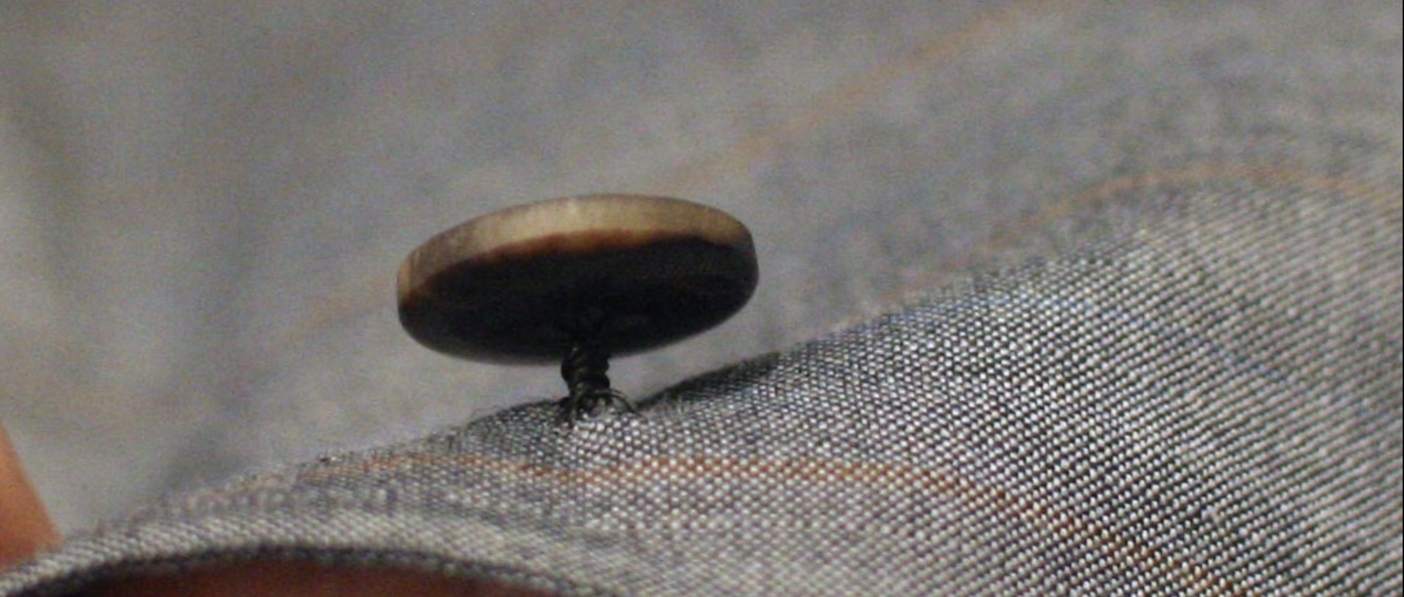 Un bouton cousu à la main sur une veste, le bouton est bien droit et est solidement cousu. (source : j.diduch) 